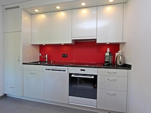 Eine moderne Küche mit weißen Schränken, einer roten Rückwand und eingebauten Geräten, darunter eine Spülmaschine und ein Backofen.
