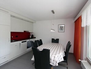 A compact kitchen with white cabinets, a red countertop, and a dining area with a checkered tablecloth and black chairs. - Tgesa La Niva 11 Appartement/Fewo, Bad, WC, 2 Schlafräume by Interhome (Savognin)