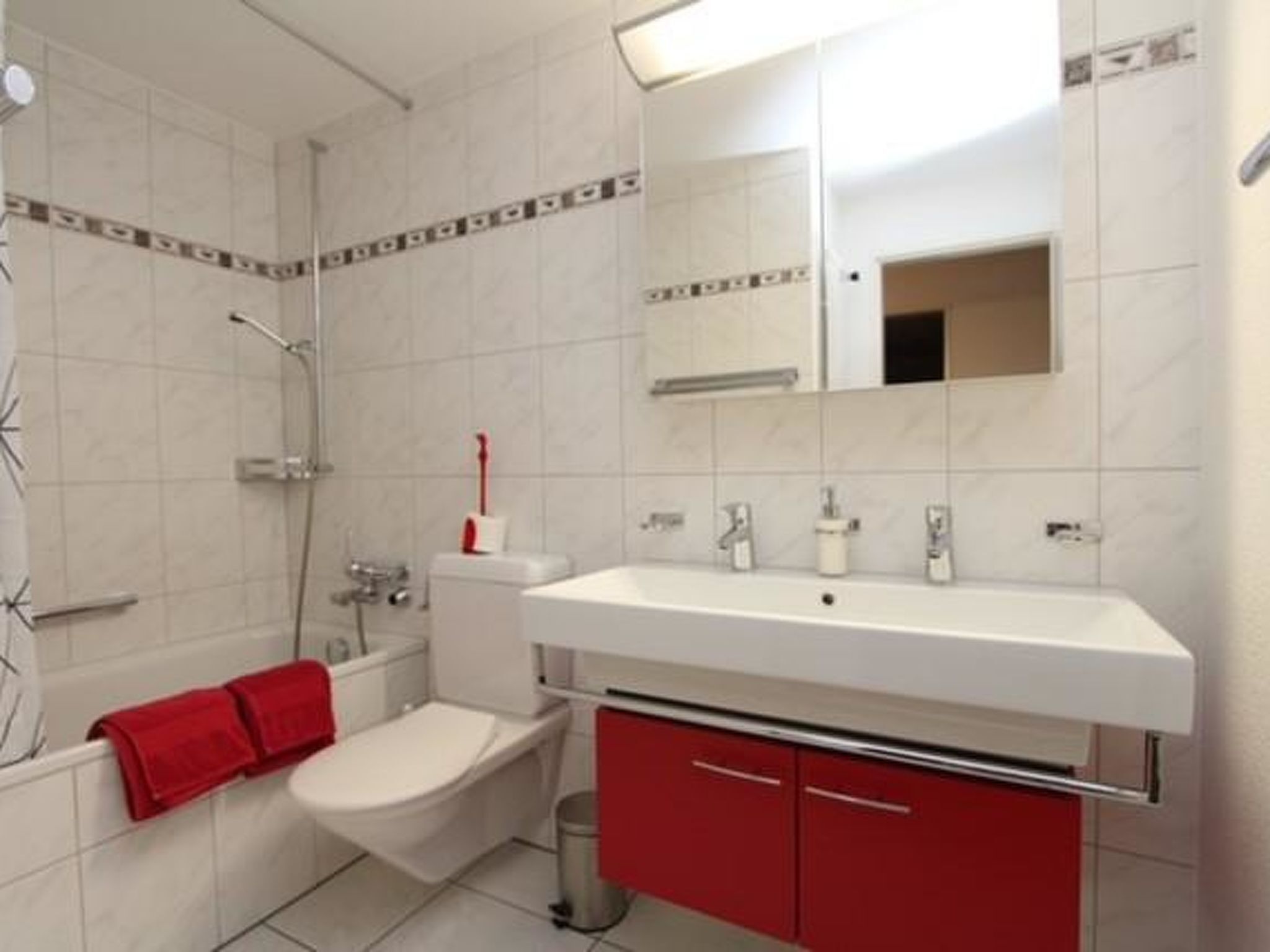 Un bagno con un lavandino bianco, mobili rossi, un water e una doccia.