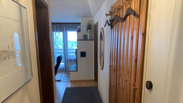 A hallway with a wooden door, a dark mat, and a view into a room with a chair and a window. - Casa Surselva Whg Bilger Appartement/Fewo, Bad, WC, 2 Schlafräume by Interhome (Savognin)