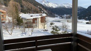A view from a balcony with a snow-covered landscape, a mountain in the background, and a building with a wooden facade. - Casa Surselva Whg Bilger Appartement/Fewo, Bad, WC, 2 Schlafräume by Interhome (Savognin)