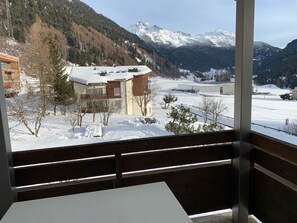 A view from a balcony with a snow-covered landscape, a mountain in the background, and a building with a wooden facade. - Casa Surselva Whg Bilger Appartement/Fewo, Bad, WC, 2 Schlafräume by Interhome (Savognin)