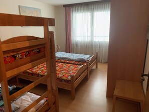 A room with two wooden bunk beds, a small table, a window with sheer curtains, and a painting on the wall. - Casa Surselva Whg Bilger Appartement/Fewo, Bad, WC, 2 Schlafräume by Interhome (Savognin)