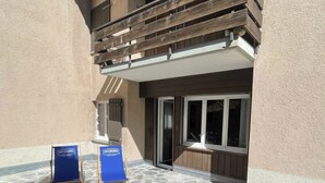 A stone patio area with two blue signs, a wooden deck, and a building with a balcony. - Appartamento Wyss Appartement/Fewo, Bad, WC, 3 Schlafräume by Interhome (Bivio)