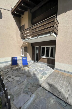 Eine gepflasterte Terrasse mit zwei blauen Schildern, einem Holzdeck und einem Gebäude mit Balkon.