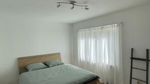A bedroom with a wooden bed, white walls, a ceiling light fixture, and a window with sheer curtains. - Appartamento Wyss Appartement/Fewo, Bad, WC, 3 Schlafräume by Interhome (Bivio)