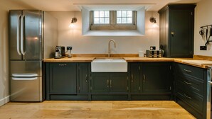 A modern kitchen with dark cabinetry, a stainless steel refrigerator, a built-in sink, and a window above the sink. - Heather View Chapel (Bradwell)