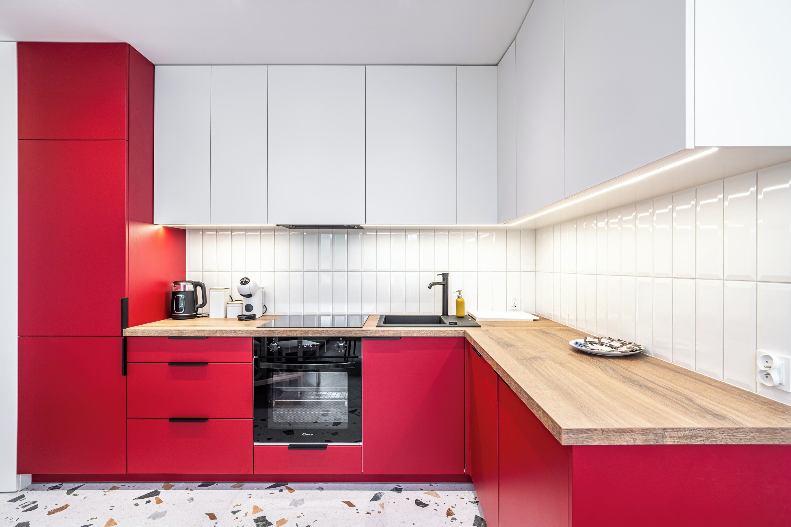A modern kitchen with red cabinetry, a black oven, a coffee maker, and a sink.