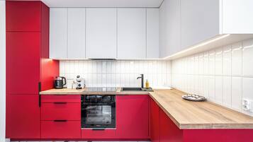 Una cocina moderna con armarios rojos, un horno negro, una cafetera y un lavabo.