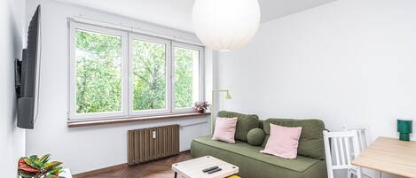 Una sala de estar moderna con un sofá verde, una mesita, un televisor y un ventanal con vistas a árboles.