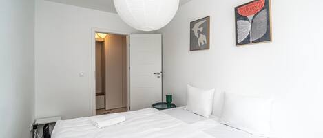 Un dormitorio con cama, una puerta, una obra de arte colgada en la pared y una lámpara en el techo.