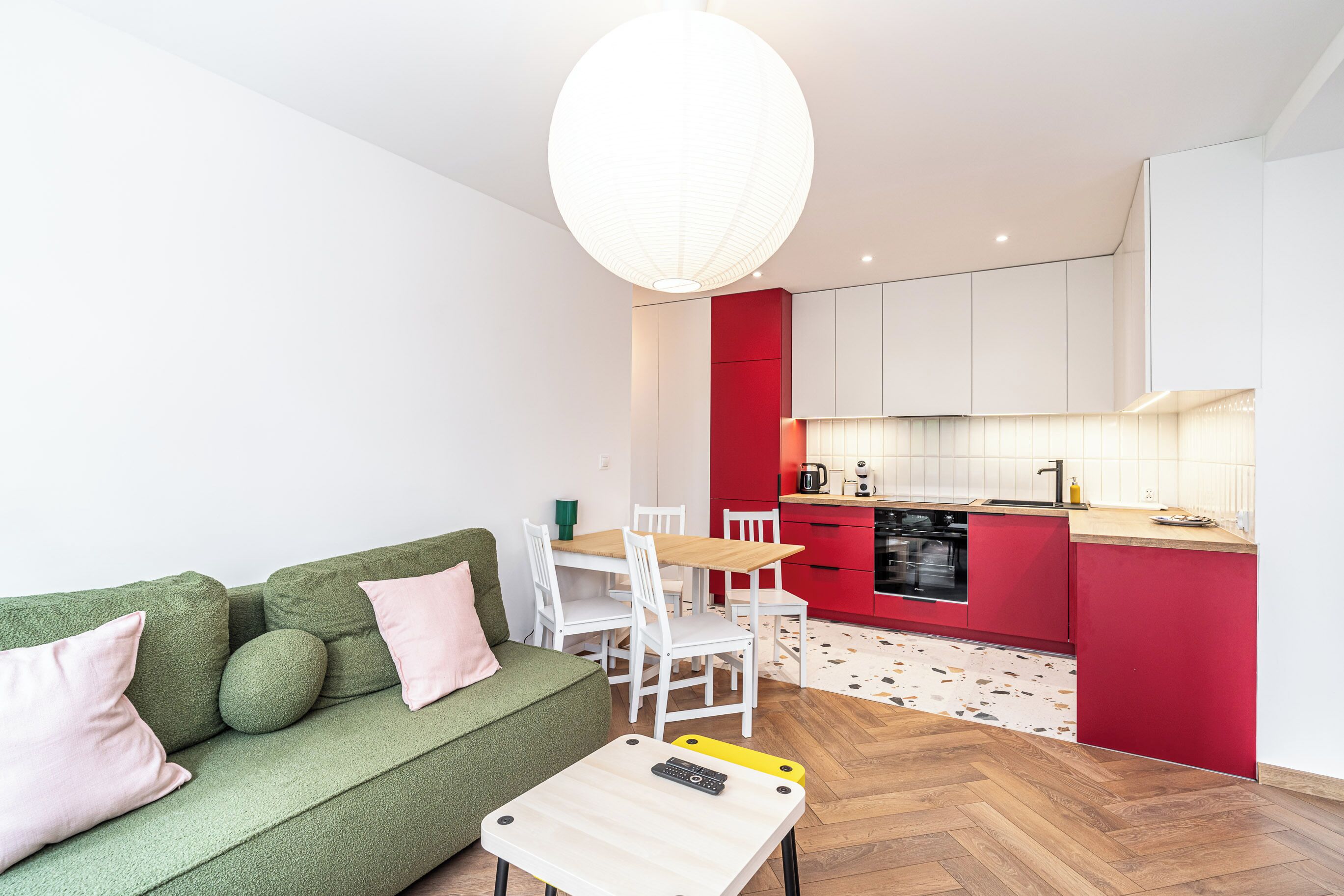 Un apartamento moderno con un sofá verde, una mesa de comedor blanca y armarios de cocina rojos.