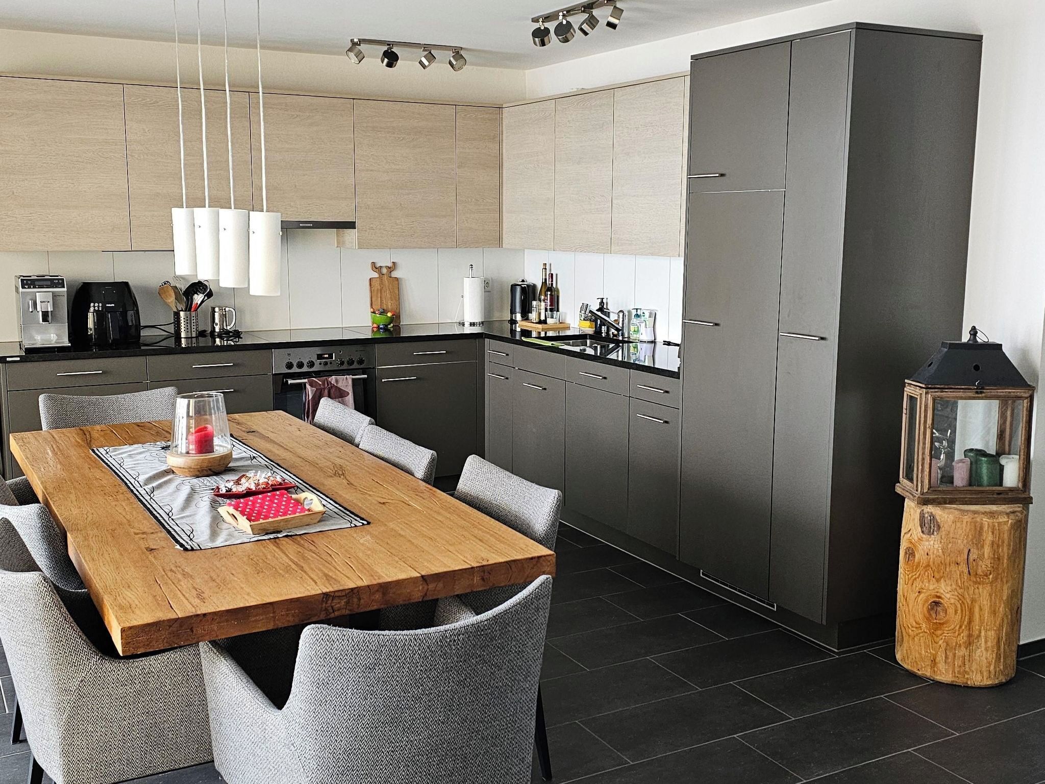 A modern kitchen with a central island, grey cabinetry, and a dining area with a wooden table and grey upholstered chairs.