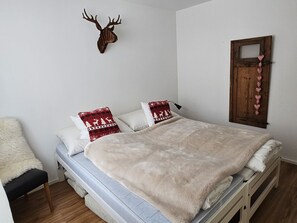 Un llit amb matalàs blanc, dos almoinos i una manta blanca i esponjosa, i un panell de fusta al capçal.