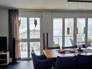 A modern dining area with a large window, a flat-screen TV, and a table set for two. - Casa a Sulegl Jacober Appartement/Fewo, Dusche und Bad, WC, 2 Schlafräume by Interhome (Savognin)