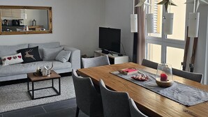 Uma sala moderna com um sofá cinzento, uma mesa de jantar de madeira e uma televisão.