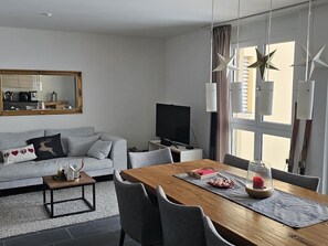 Ein modernes Wohnzimmer mit einem grauen Sofa, einem Holzesstisch und einem Fernseher.