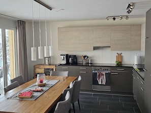 A modern kitchen with a wooden dining table, grey cabinets, and a built-in oven.