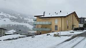 Um edifício com várias andares e varandas, paisagem coberta de neve e uma estrada ao primeiro plano.