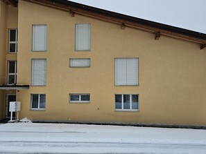 A building with multiple windows, some with blinds, and a snow-covered ground.