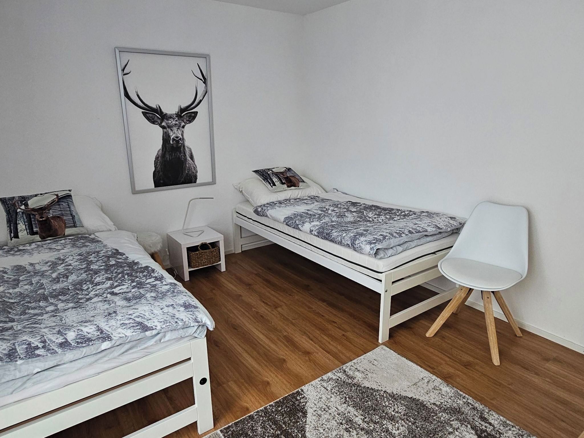 Une chambre avec deux lits, une table de chevet, une chaise, un tapis et une décoration murale représentant des bois de cerf.