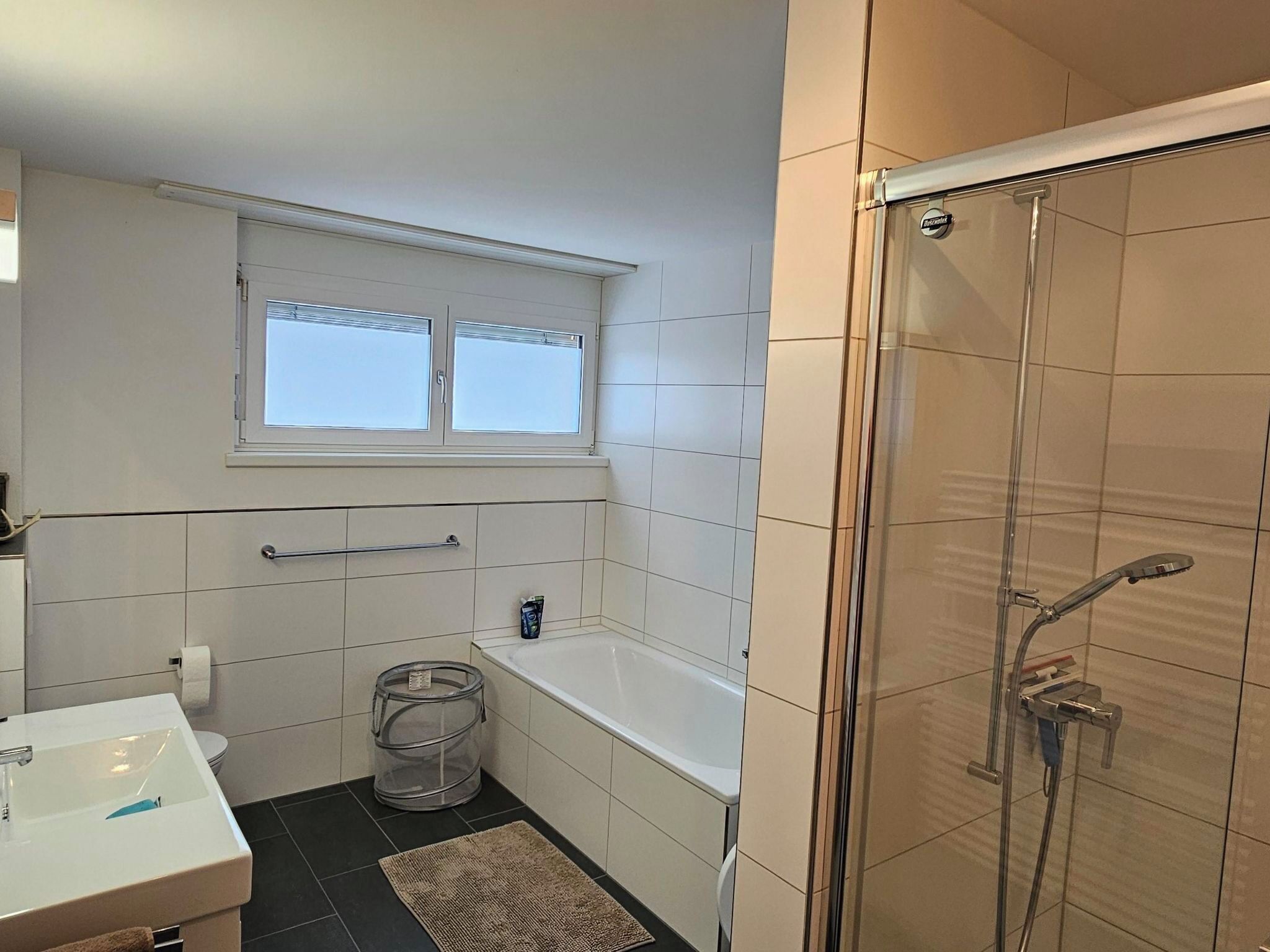 Et badeværelse med badekar, bruser, toilet, vask og et vindue.