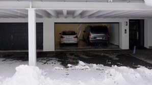Un garaje cubierto con dos coches aparcados en su interior, nieve en el suelo y una puerta parcialmente visible a la derecha.