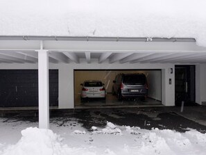 A covered parking garage with two cars parked inside, snow on the ground, and a partially visible door on the right. - Casa Stella Appartement/Fewo, Dusche, WC, 2 Schlafräume by Interhome (Savognin)