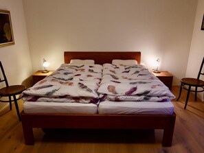 A double bed with a floral bedspread, two bedside tables with lamps, and a wooden floor. - Casa Stella Appartement/Fewo, Dusche, WC, 2 Schlafräume by Interhome (Savognin)