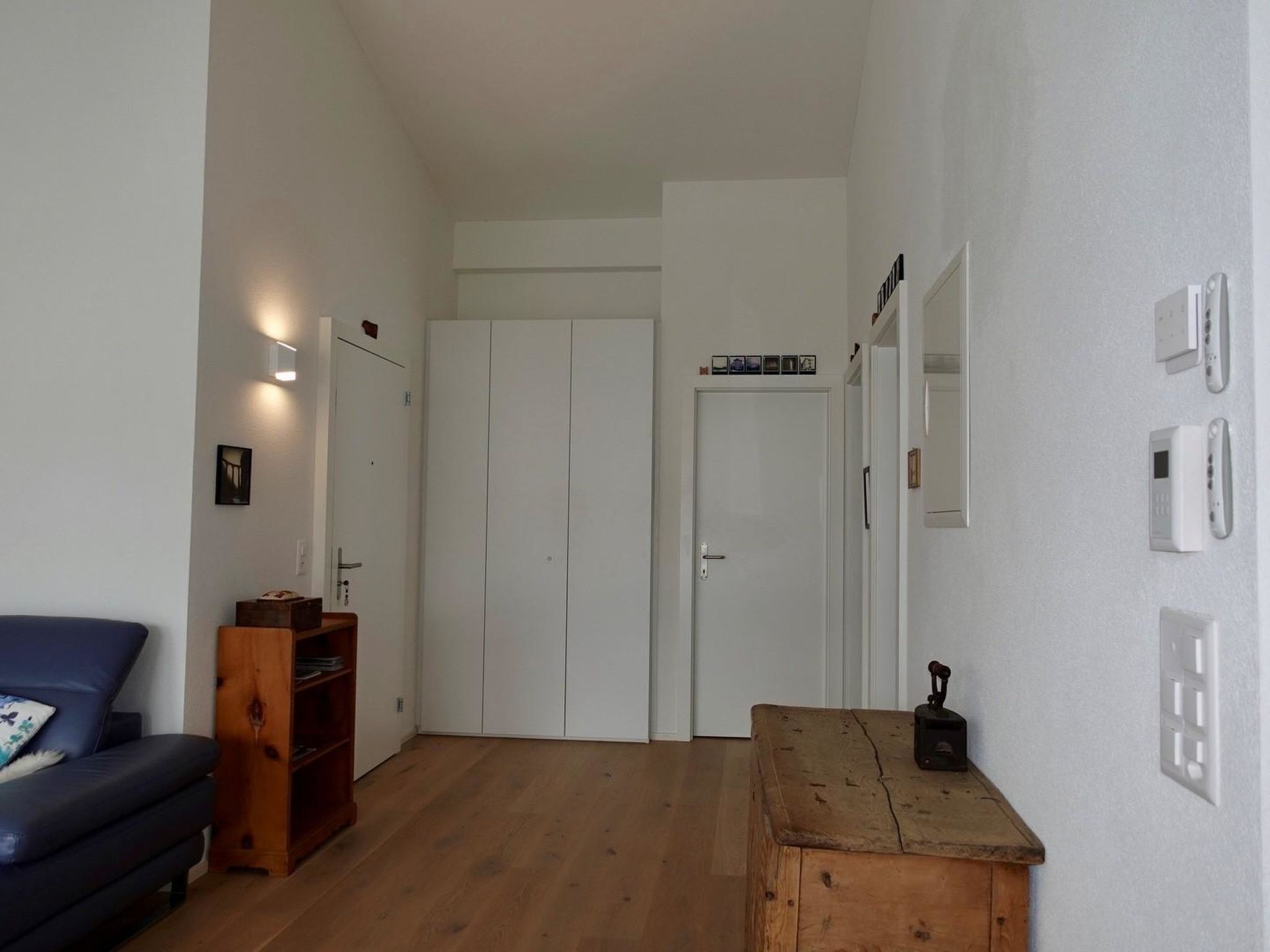 Una stanza con una panca di legno, un divano blu, un armadio e una porta che dà su un'altra stanza.