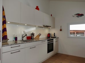 A modern kitchen with white cabinets, a stainless steel range hood, a red kettle, and a window with a view of a vehicle outside. - Casa Stella Appartement/Fewo, Dusche, WC, 2 Schlafräume by Interhome (Savognin)
