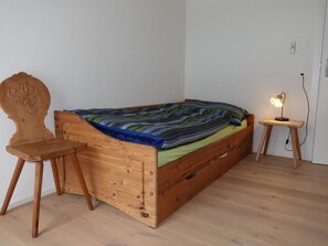 A single bed with a wooden frame, a small bedside table with a lamp, and a chair with a carved backrest. - Casa Stella Appartement/Fewo, Dusche, WC, 2 Schlafräume by Interhome (Savognin)