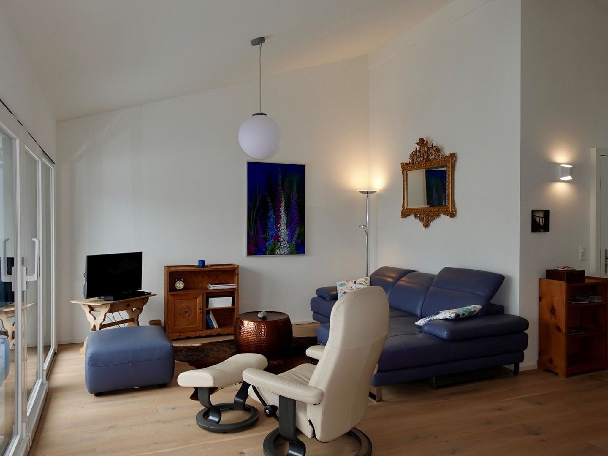 Uma sala de estar moderna com um sofá, uma poltrona, uma televisão e um quadro na parede.