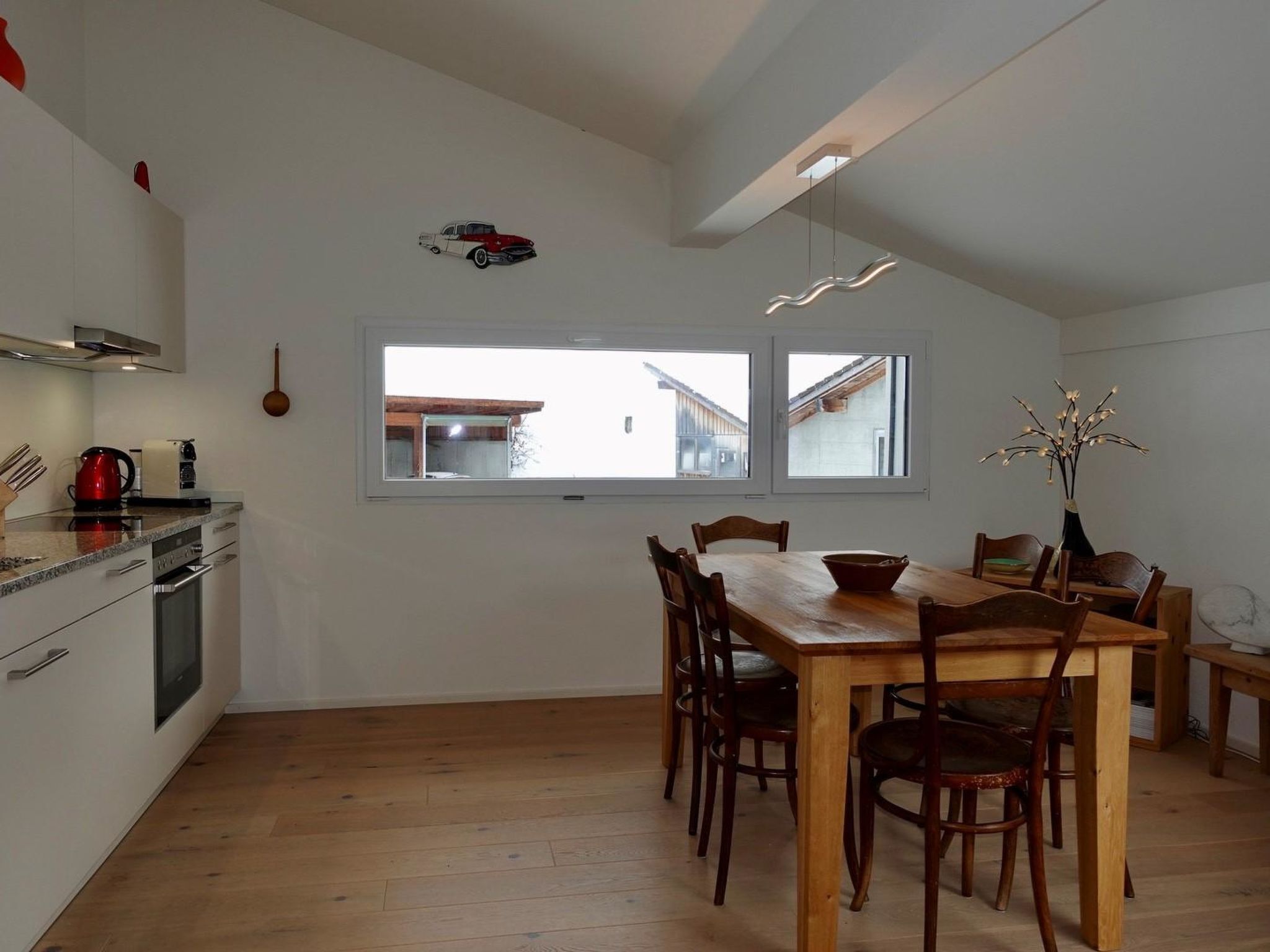 Una cucina moderna con zona pranzo, pavimento in legno e una finestra che dà su un edificio.