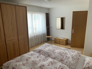 A bedroom with a bed, a wardrobe, a dresser, a mirror, and a window with curtains. - Tgesa Marlotscha Appartement/Fewo, Dusche oder Bad, WC, 3 Schlafräume by Interhome (Savognin)