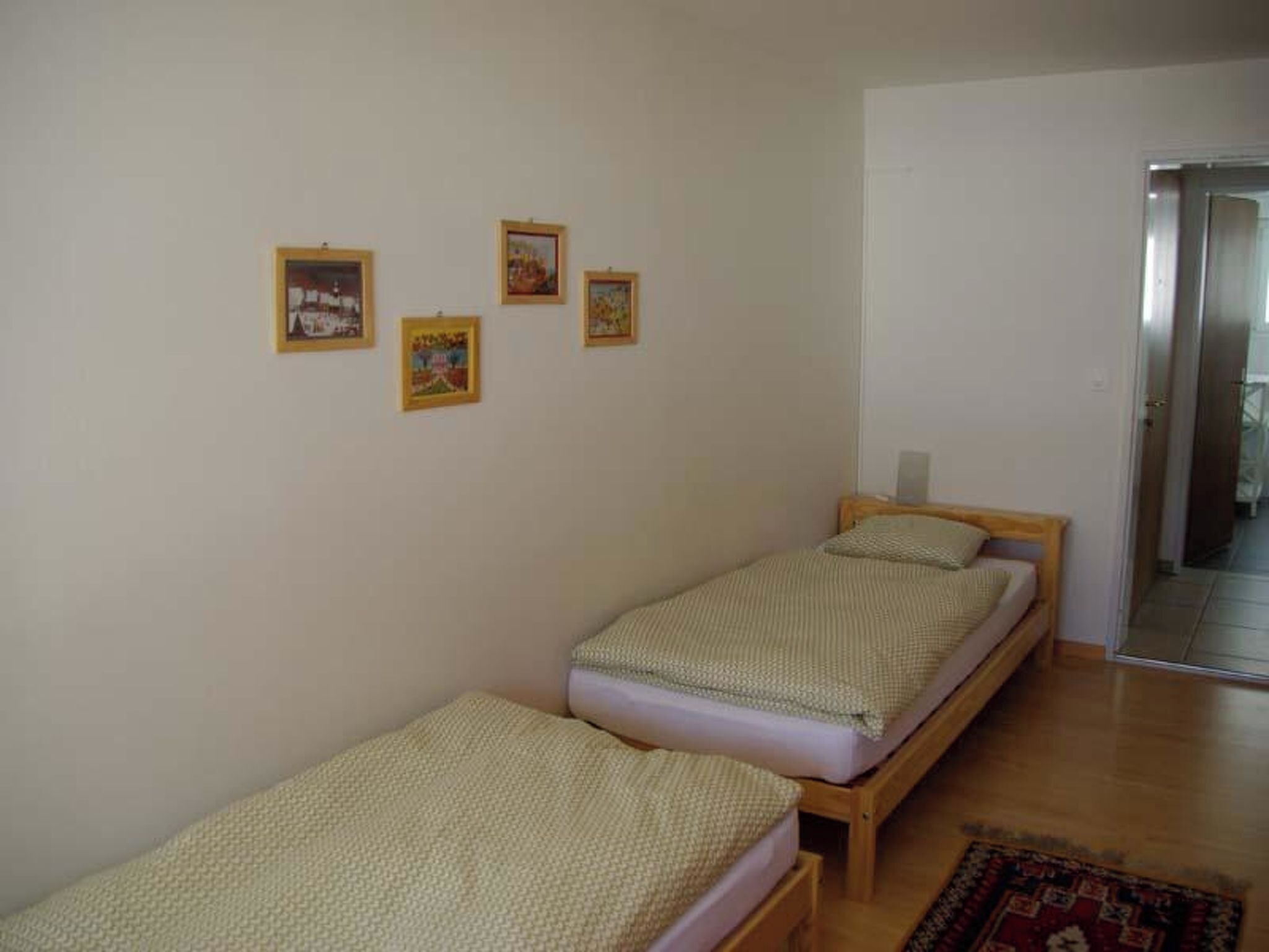 Ein Zimmer mit zwei Einzelbetten, Holzboden und einer Tür zu einem weiteren Raum.