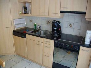 A kitchen with wooden cabinets, a black countertop, a coffee maker, and a dishwasher. - Tgesa Marlotscha Appartement/Fewo, Dusche oder Bad, WC, 3 Schlafräume by Interhome (Savognin)