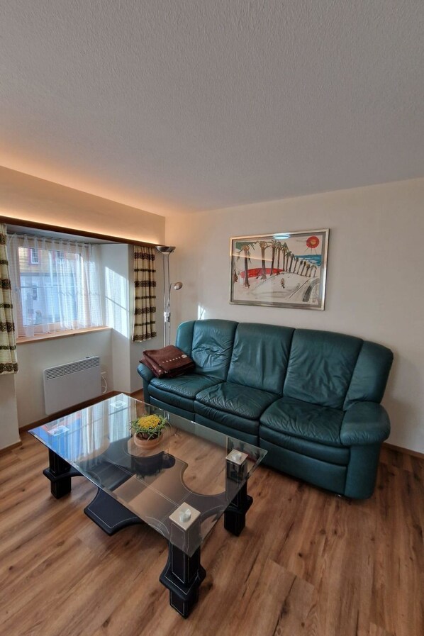 Una sala de estar con un sofá verde, una mesa de centro de vidrio y un cuadro en la pared.