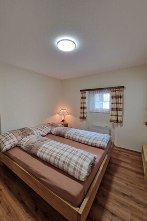 A room with a bed, a lamp, a window with curtains, and a radiator. - Haus Rizzi Appartement/Fewo, Dusche, WC, 1 Schlafraum by Interhome (Bivio)