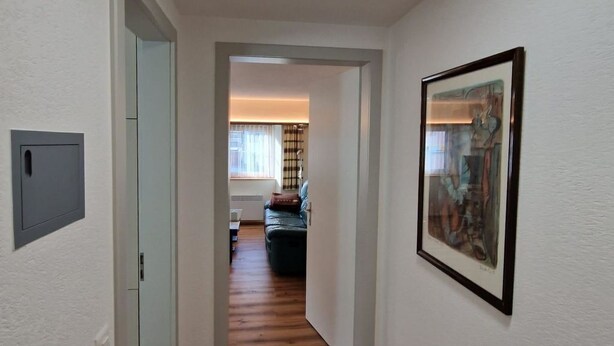 A hallway with a wooden floor, a ceiling light, a door on the left, and a framed picture on the right. - Haus Rizzi Appartement/Fewo, Dusche, WC, 1 Schlafraum by Interhome (Bivio)