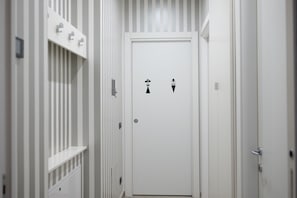 A narrow hallway with a white door featuring restroom symbols. - An elegant and welcoming 80-square-meter apartment, perfect for three people, located on the raised ground floor of an upscale building.The property is ideally situated for exploring the city: the Royal Villa of Monza is just a 10-minute walk away, while (Monza)