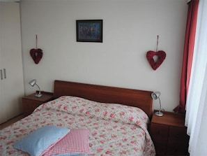 Et soveværelse med en seng, to sengeborde, en lampe på hvert bord, et billede på væggen og to hjerteformede dekorationer.
