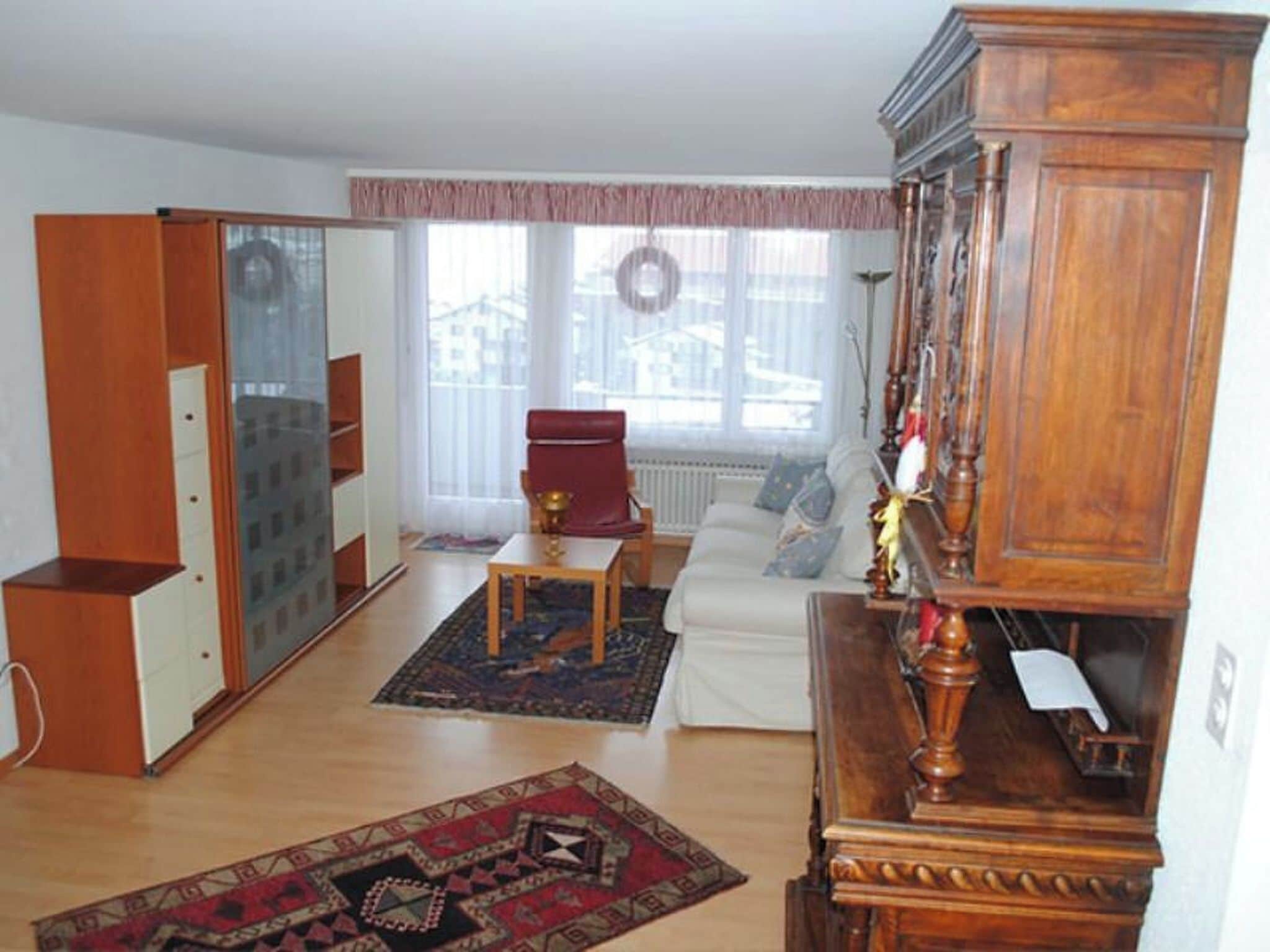 A living room with a sofa, a red chair, a wooden cabinet, and a patterned rug.