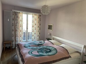 Ein Schlafzimmer mit einem Bett, einem Heizkörper, einem Fenster mit Vorhängen und einer Pendelleuchte.