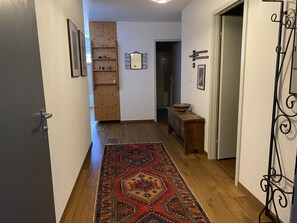 Ein Flur mit Holzboden, einem gemusterten Teppich, einem Holzschrank und einer Tür mit Metallbeschlag.