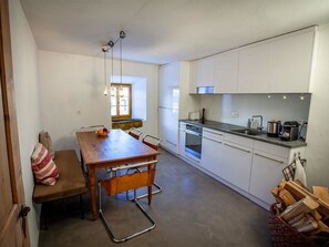 A compact kitchen with white cabinets, a dining table with chairs, and a window providing natural light. - Tgesa Antgerna 1.OG Appartement/Fewo, Bad, WC, 2 Schlafräume by Interhome (Salouf)