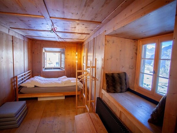 A wooden cabin room with a bed, a bench, a window with a view, and a radiator.