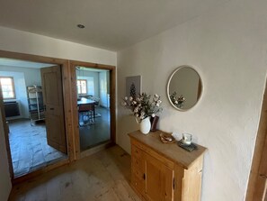 A room with a wooden dresser, a mirror, and a vase with flowers. There is a door leading to another room with a table and chairs. - Tgesa Antgerna 1.OG Appartement/Fewo, Bad, WC, 2 Schlafräume by Interhome (Salouf)