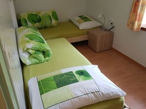 A small, single-room accommodation with two beds, each with green leaf-patterned bedding. - Tga Mucki Appartement/Fewo, Dusche oder Bad, WC, 2 Schlafräume by Interhome (Savognin)