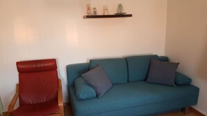 Um quarto com uma cadeira vermelha, um sofá azul com almofadas e piso de madeira.